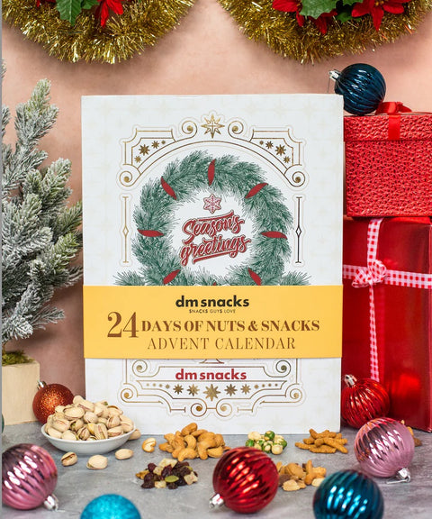 "24 Days of Nuts & Snacks Advent Calendar with festive packaging and a variety of holiday treats displayed around it"