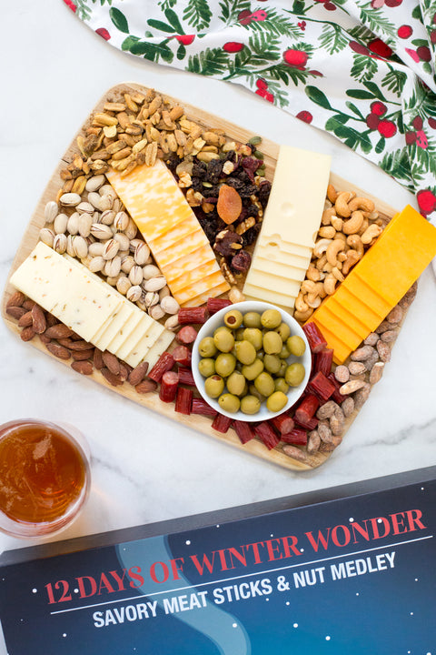 Gourmet advent calendar with savory meat sticks, nut medley, cheese, and olives on a festive platter for holiday celebration.