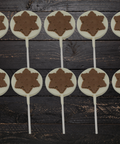 Festive milk and white chocolate snowflake lollipops set on a rustic wooden table, perfect for Christmas gifting and stocking stuffers.