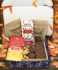 Autumn Assortment Box with fall chocolates, pumpkin spice almonds, and maple bourbon pecans on a table with leaves.