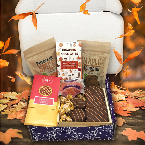 Autumn Assortment Box with fall chocolates, pumpkin spice almonds, and maple bourbon pecans on a table with leaves.