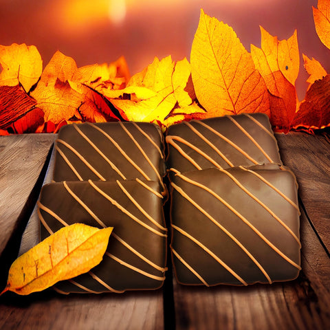 Fall-themed chocolate squares with an orange drizzle, surrounded by autumn leaves on a wooden table background.