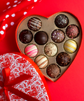 Heart-shaped Valentine's Day chocolate truffle box with assorted flavors on a red background.