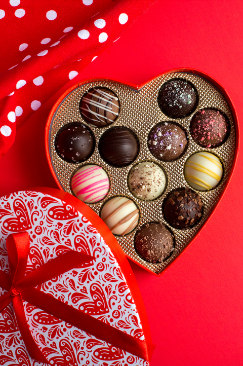 Heart-shaped Valentine's Day chocolate truffle box with assorted flavors on a red background.