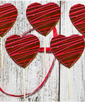 Chocolate heart lollipops with red and pink drizzle, set of 5, on rustic wood background with red ribbon.