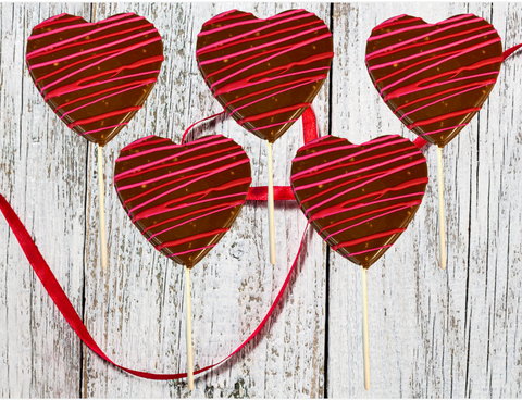 Chocolate heart lollipops with red and pink drizzle, set of 5, on rustic wood background with red ribbon.