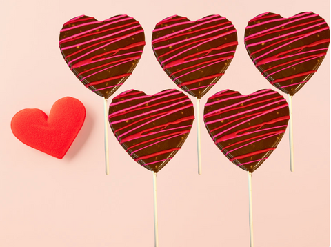 Chocolate heart lollipops with red and pink drizzle, set of 5, on a pink background with a red heart decoration.