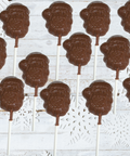 Milk chocolate Santa lollipops arranged on white wooden background with snowflake accents, ideal for Christmas gifts and treats.