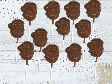 Milk chocolate Santa lollipops arranged on white wooden background with snowflake accents, ideal for Christmas gifts and treats.