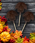 Chocolate turkey lollipops surrounded by autumn leaves, pumpkins, and red berries, perfect for Thanksgiving festivities and gifting.