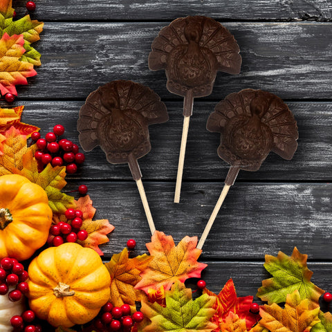 Chocolate turkey lollipops surrounded by autumn leaves, pumpkins, and red berries, perfect for Thanksgiving festivities and gifting.