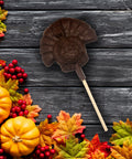 Chocolate turkey lollipop on wooden table with autumn leaves and mini pumpkins, part of the Thanksgiving Nut Tray gift set.