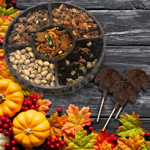 Thanksgiving nut tray with gourmet snacks and chocolate turkey lollipops, surrounded by autumn leaves and pumpkins.