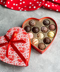 Heart-shaped box of assorted Valentine’s Day truffles, featuring elegant designs, with a red ribbon and polka dot cloth.