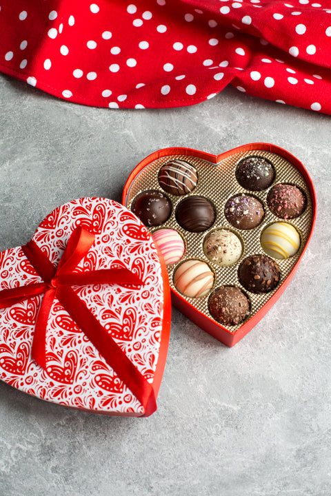 Heart-shaped box of assorted Valentine’s Day truffles, featuring elegant designs, with a red ribbon and polka dot cloth.