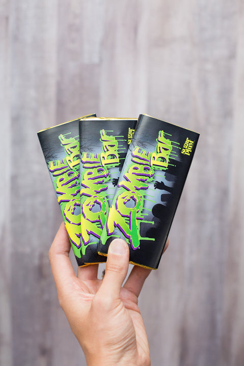 Hand holding three Chocolate Zombie Bars with vibrant green and purple packaging, perfect Halloween candy for parties and trick-or-treaters.